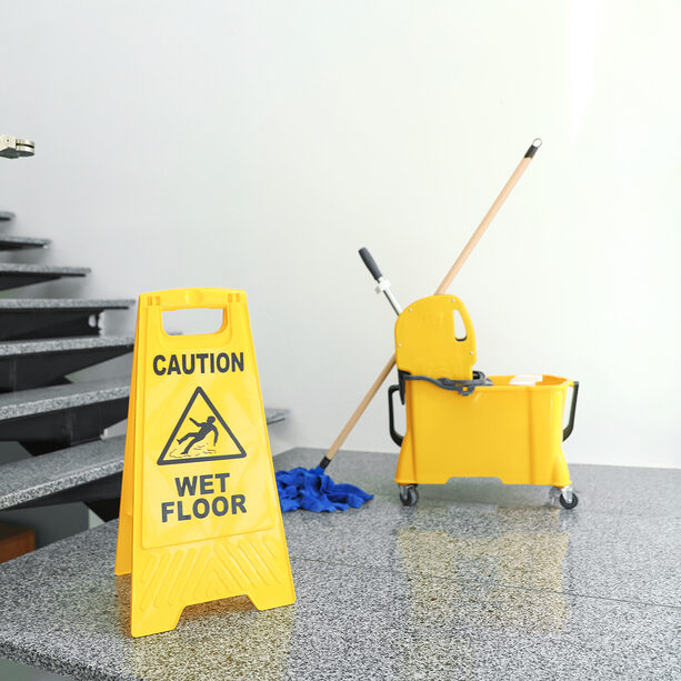 Safety sign with phrase "CAUTION WET FLOOR" and mop bucket on stairs. Cleaning tools